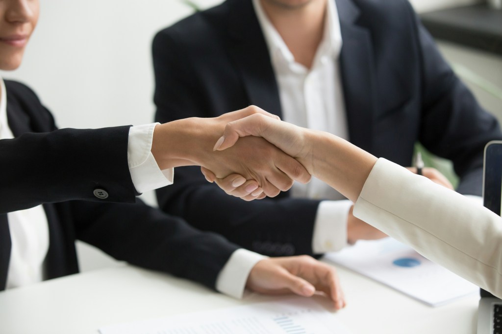 Two businesswomen shaking hands across a desk after a meeting