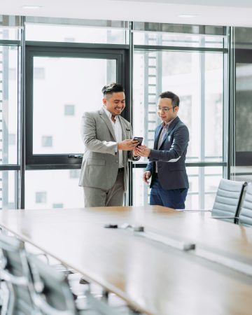 Two businessmen in suits reviewing something on a smartphone in a boardroom